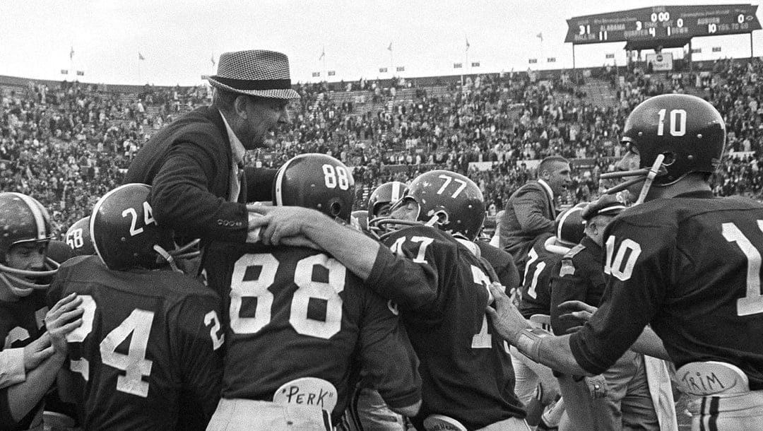 Black and white photograph of an Alabama coach in a houndstooth hat carried on his players' shoulders, the scoreboard behind reading Alabama 31 Auburn 7