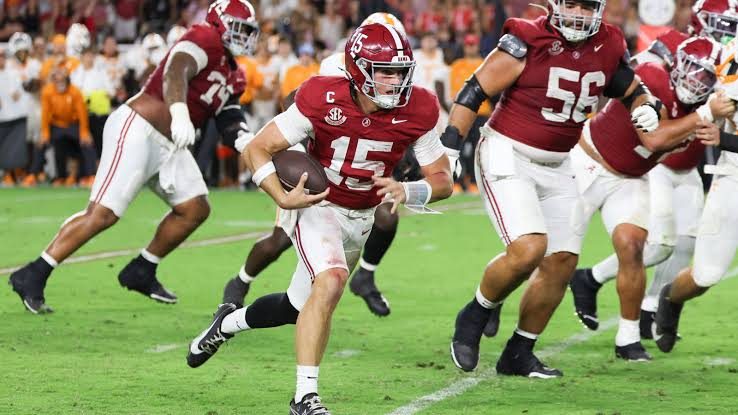 An Alabama quarterback in crimson scrambling out of the pocket behind his offensive line against Tennessee