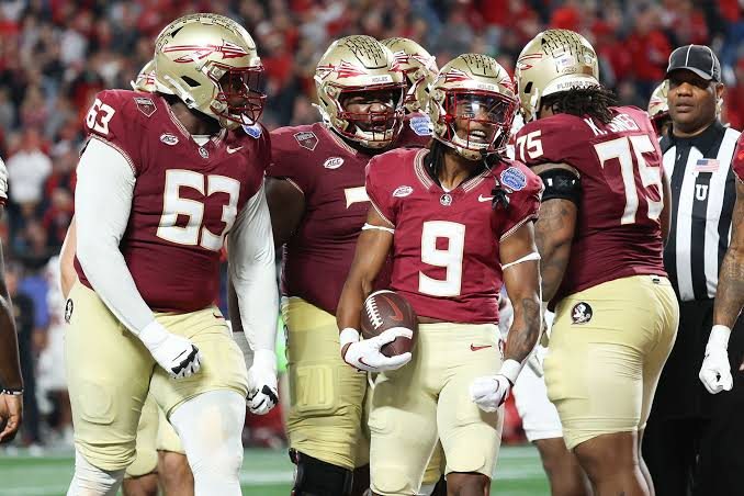 Florida State Seminoles football players wearing garnet and gold jerseys celebrating together on the field during an exciting moment in game action, showing team passion and excitement.