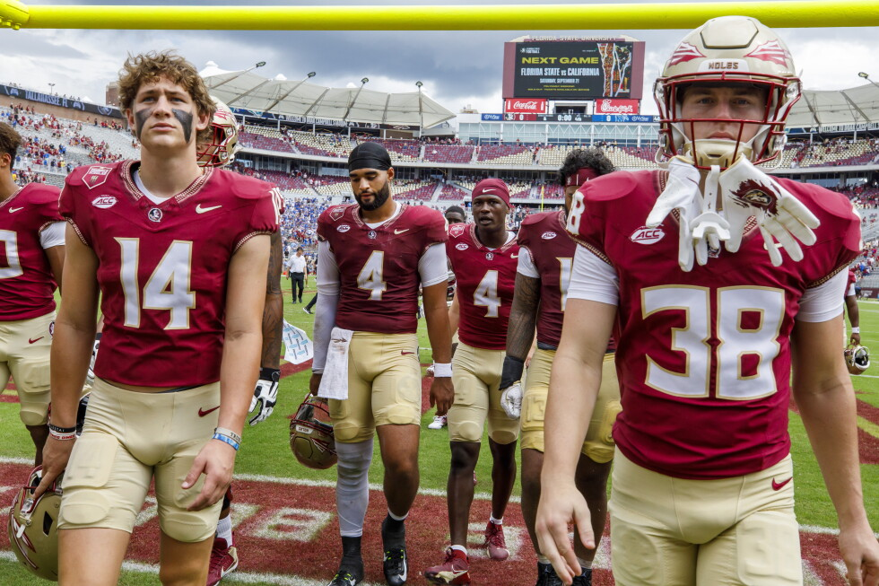 Florida State Seminoles players and coaching staff standing along the sideline at Doak Campbell Stadium during a game, observing the action and preparing for the next play.
