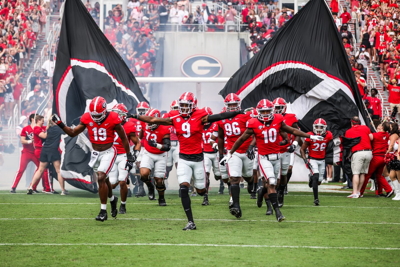 Georgia players in red jerseys sprinting onto the field through smoke between two large black and red team flags