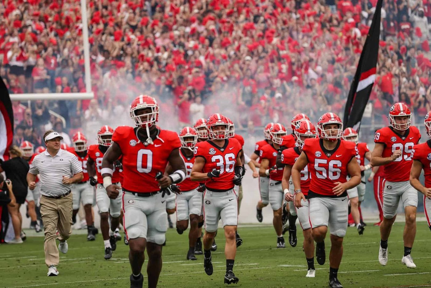Georgia players running onto the field led by their head coach in a white cap and shirt