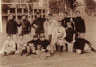 Sepia photograph of an early Louisiana State football squad posed on a field in heavy knit sweaters, one player holding a ball and a dog seated in front of the group