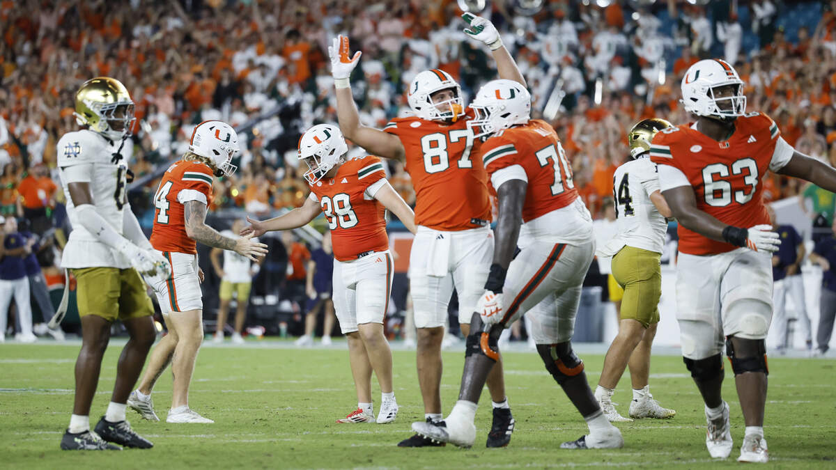 Miami Hurricanes football players wearing orange and green jerseys celebrating together on the field during an exciting moment in the game, showing team confidence and dominance.