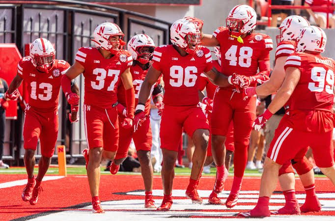 Nebraska players in red uniforms celebrating together in the end zone at Memorial Stadium