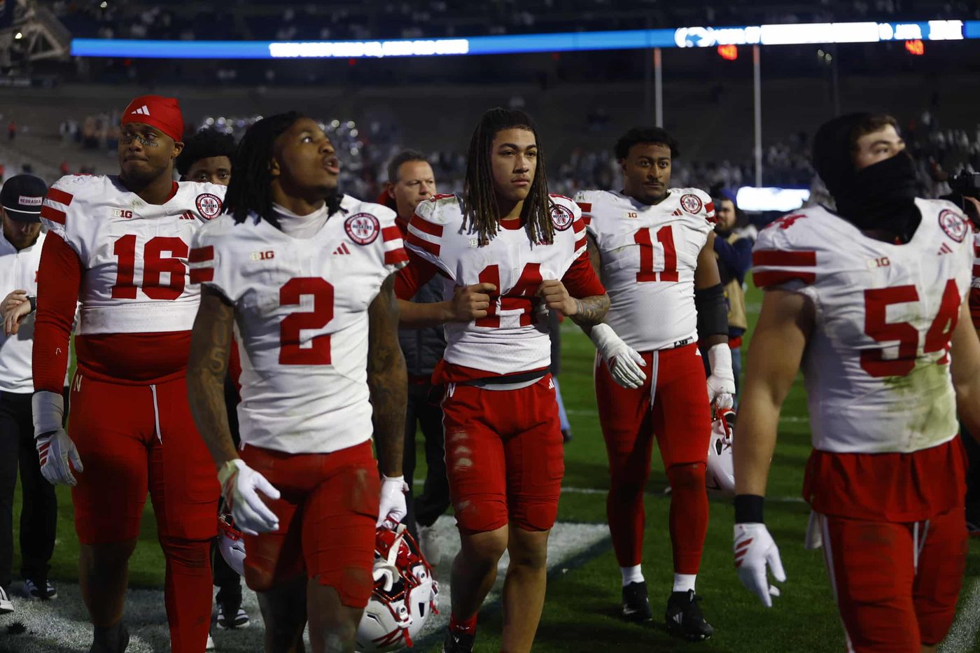 Nebraska players in white road uniforms walking off the field together after a night game