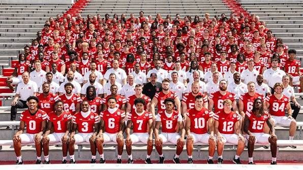 Modern Nebraska football team photograph, the full squad arranged on stadium bleachers in red and white