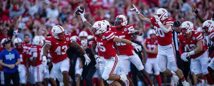 Nebraska defenders in red jerseys running and celebrating after a turnover, one holding the ball aloft