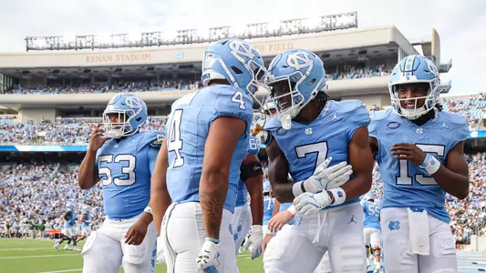 Kenan Stadium during game day with Tar Heels players actively playing on the field, fans filling the stands watching the action, and the electric atmosphere of college football in Chapel Hill.