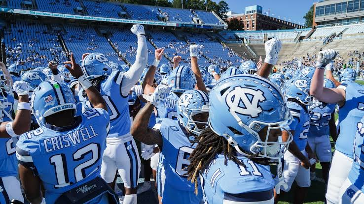 North Carolina Tar Heels players wearing light blue jerseys celebrating together on the field during game action, displaying team enthusiasm and joy after a successful play.