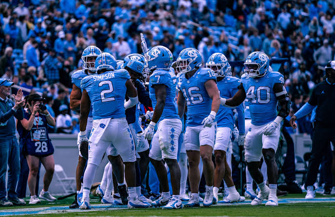North Carolina Tar Heels players gathered tightly in a huddle formation, listening to the quarterback or play-caller relay the next offensive play and preparing for execution.