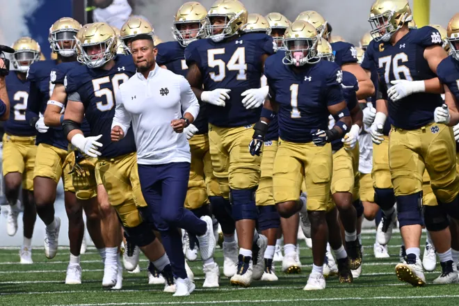Notre Dame coach with players on the sideline during a game