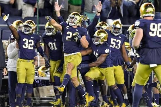 Notre Dame Fighting Irish players in navy and gold celebrating on the field during a game