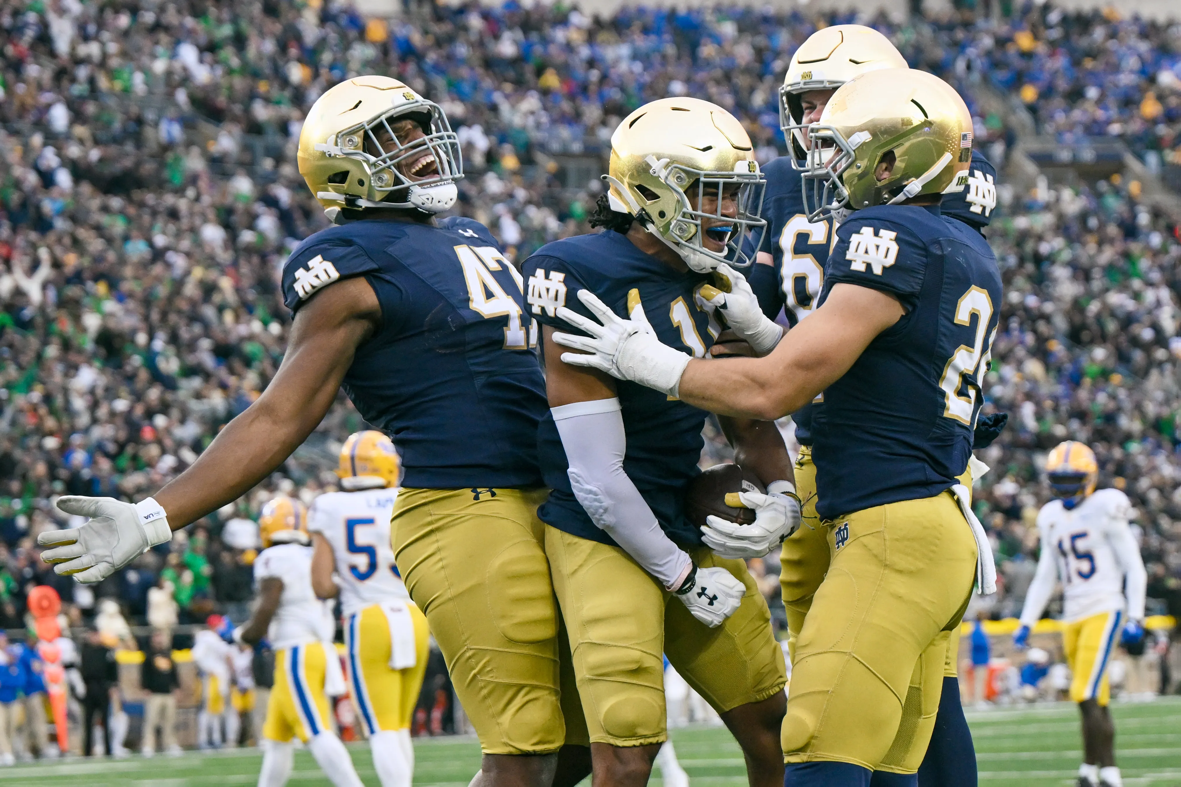 Notre Dame players in navy and gold helmets celebrating together on the field