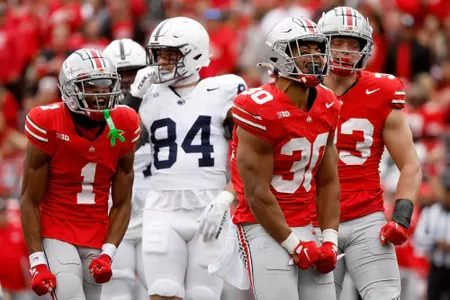 Ohio State players in scarlet home uniforms celebrating a defensive stop in front of a Penn State opponent