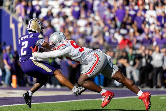 An Ohio State defender diving to tackle a Washington receiver near the sideline