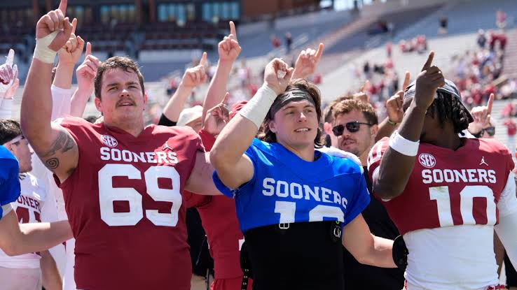 Oklahoma Sooners players in crimson jerseys celebrating together on the field