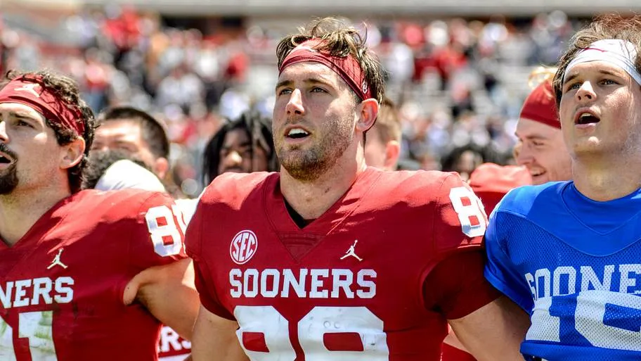 Oklahoma Sooners players in crimson jerseys on the sideline during game