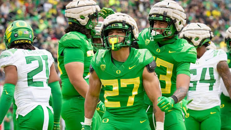 Oregon players in green uniforms celebrating a defensive stop together on the field