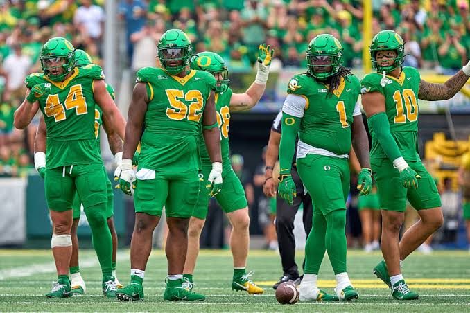 Oregon defensive linemen and linebackers standing together in all-green uniforms between plays
