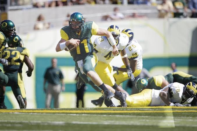 An Oregon quarterback in an early 2000s green and yellow uniform running with the ball against Michigan