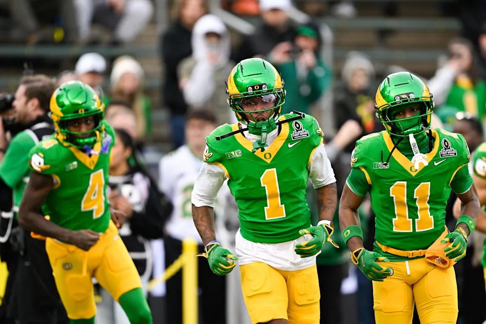 Three Oregon receivers in green and yellow uniforms jogging onto the field before a playoff game