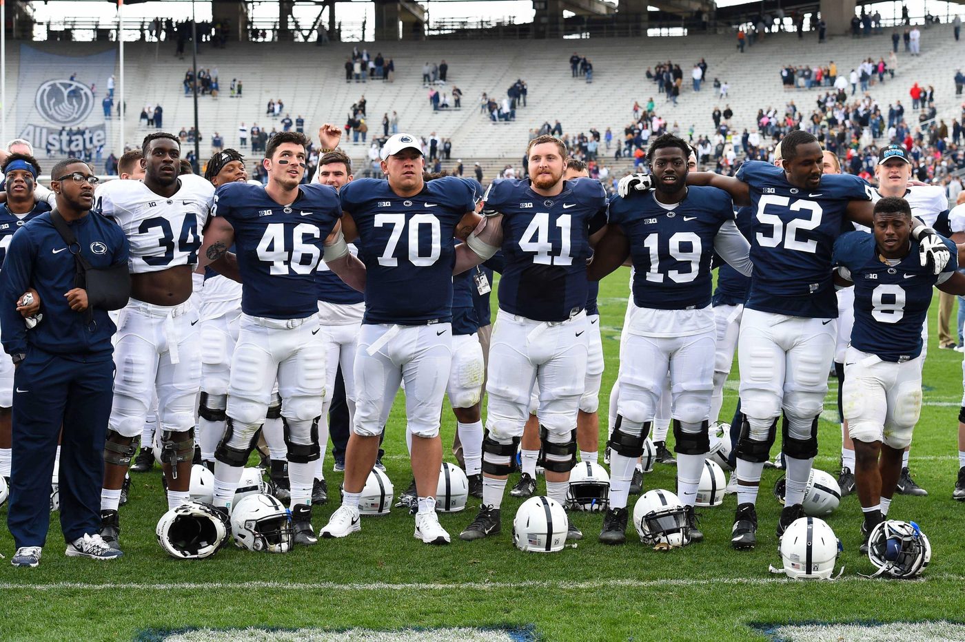 Penn State players in navy jerseys standing arm in arm across the field, facing the stands after a game at Beaver Stadium