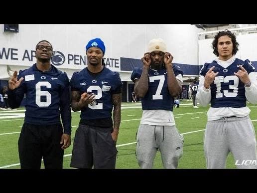 Four Penn State players standing together in the indoor practice facility in front of a We Are Penn State wall graphic