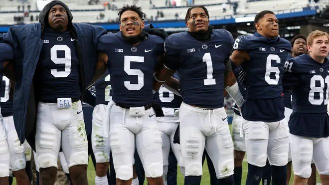 A close view of Penn State players in navy jerseys with arms across each other's shoulders, singing toward the stands