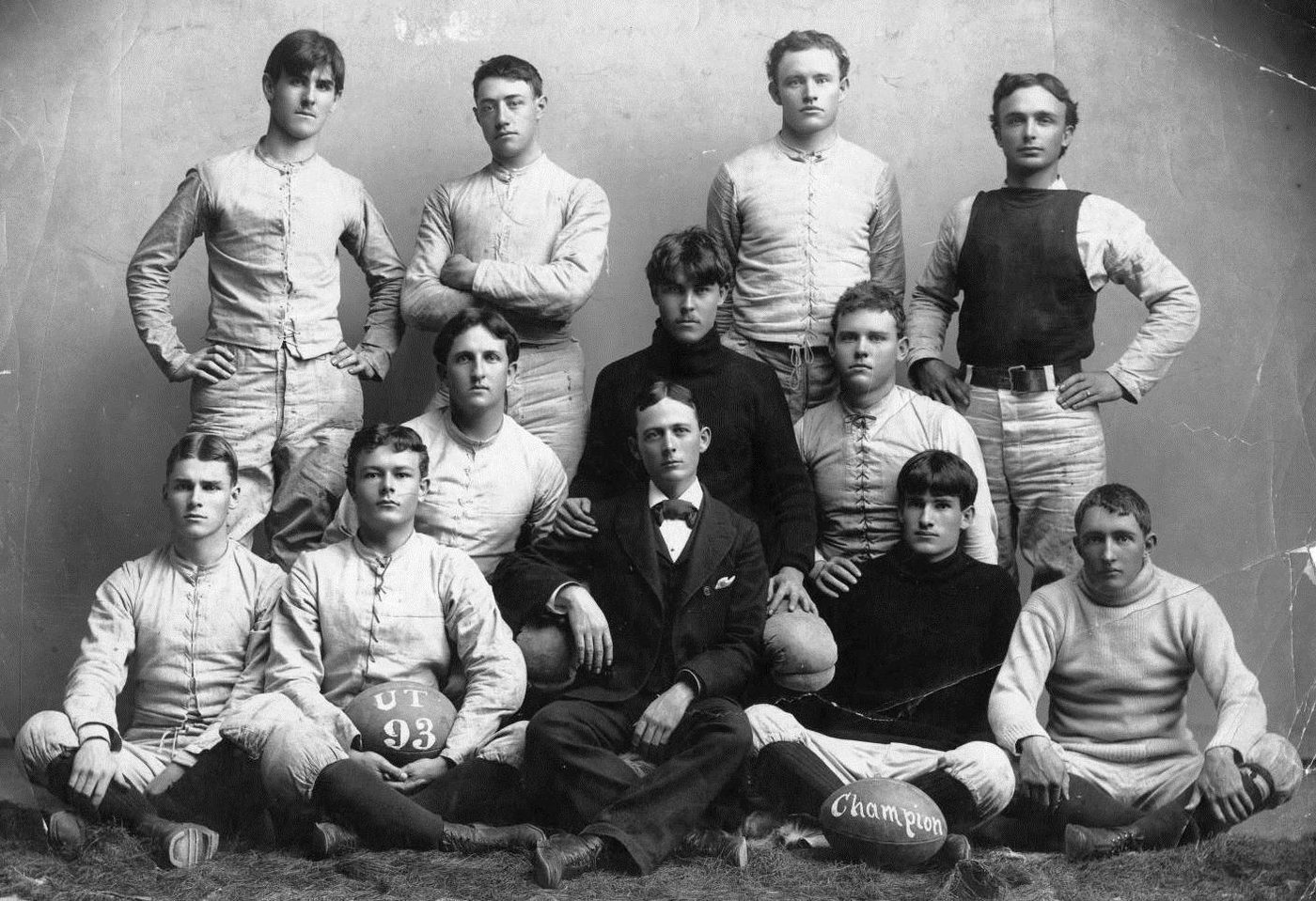 Studio portrait of the 1893 University of Texas football squad, two footballs in front of them lettered UT 93 and Champion