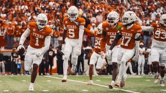Texas players in white helmets running down the field together in celebration after a turnover