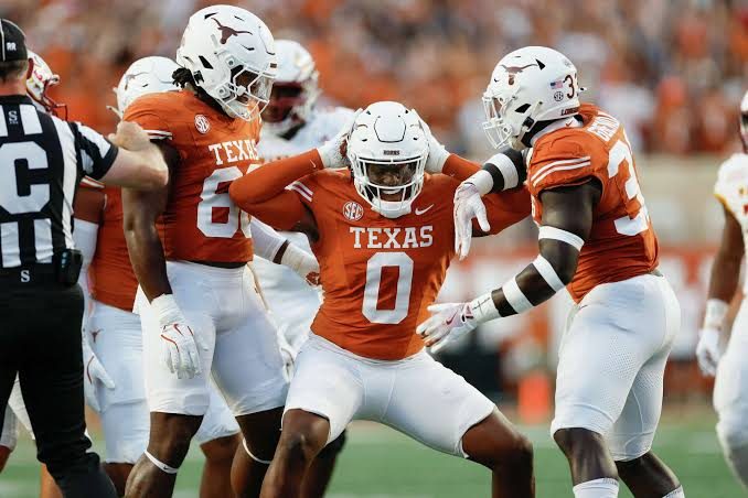 A Texas defender in burnt orange celebrating a stop with two teammates either side of him