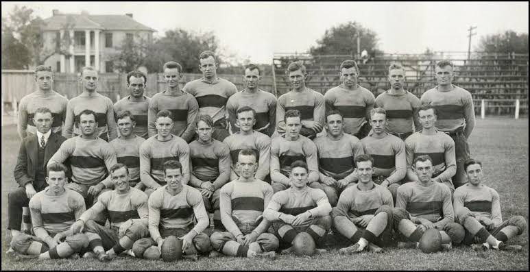Black and white team photograph of an early Texas squad in horizontally striped jerseys, seated and standing in three rows on the practice field