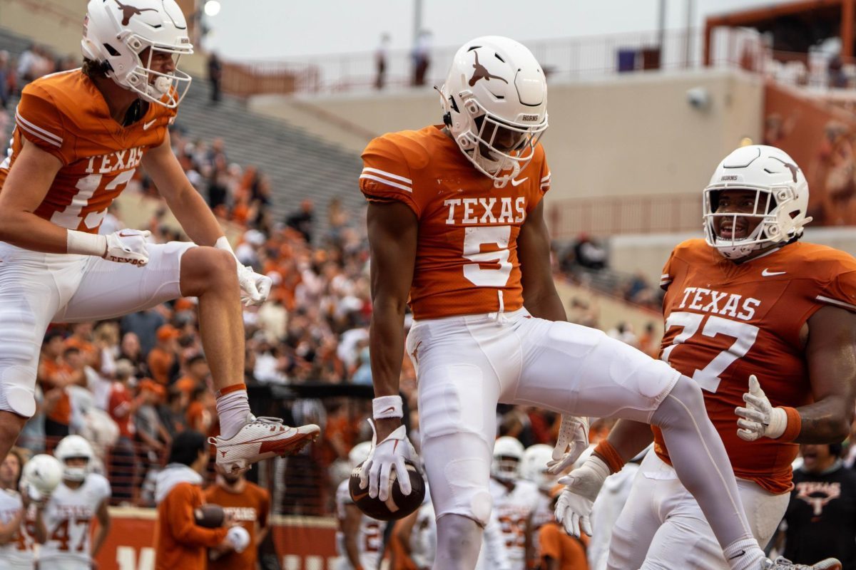 A Texas receiver in burnt orange celebrating a touchdown in the end zone as two teammates run in to join him
