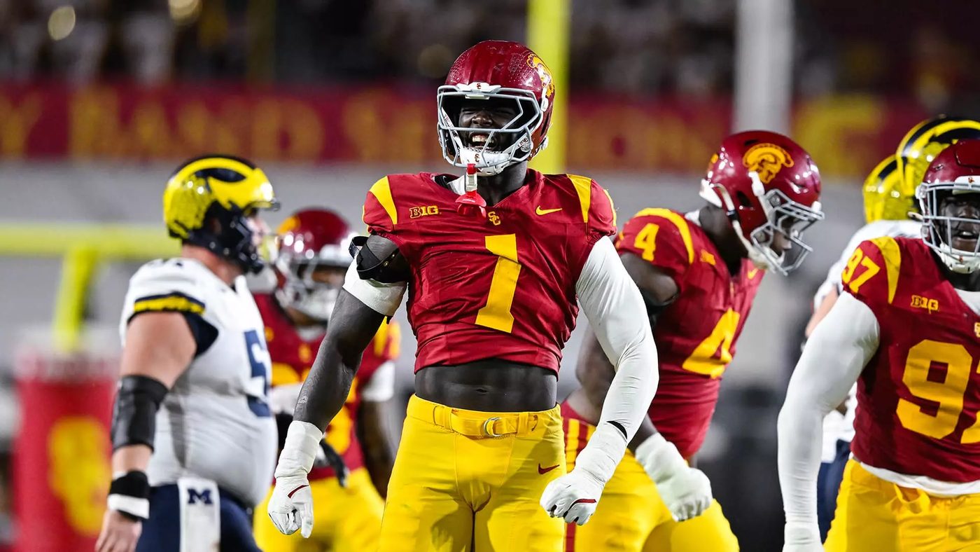 A USC defender in a cardinal jersey celebrating after a play as Michigan players in white and navy look on
