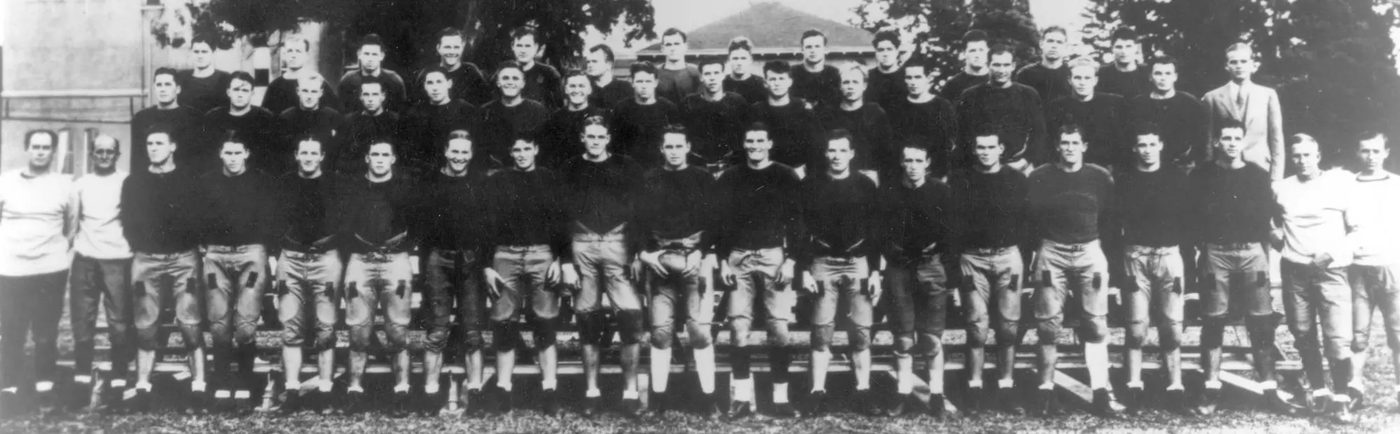 Wide black and white panoramic team photograph of an early USC squad in dark sweaters standing in three long rows outdoors